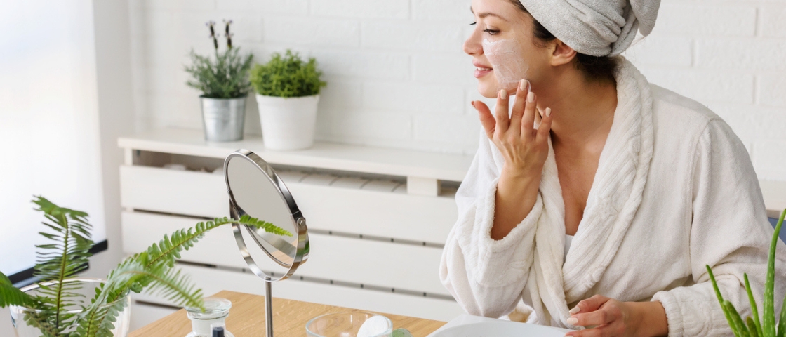 Femme en peignoir appliquant un soin visage devant un miroir, ambiance cocooning