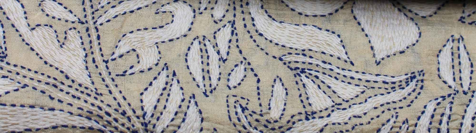 Tissu avec des motifs de broderie détaillés dans des tons bleus et beiges, avec des designs floraux et géométriques.