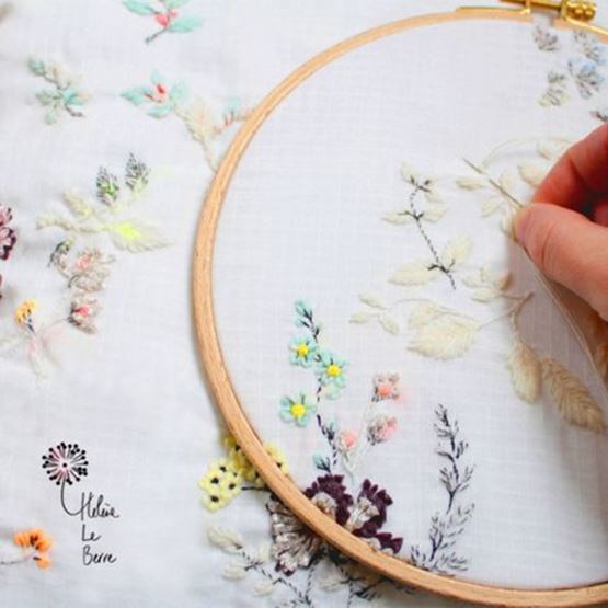 Broderie de fleurs multicolores sur du tissu blanc à l'aide d'un tambour de broderie.