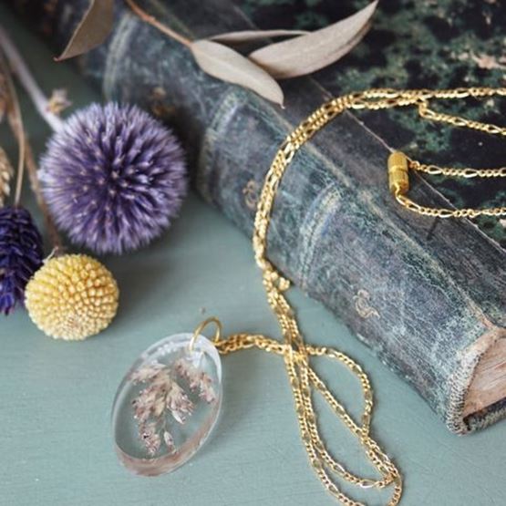 Collier doré avec pendentif en résine transparente contenant des fleurs séchées, posé sur un vieux livre.