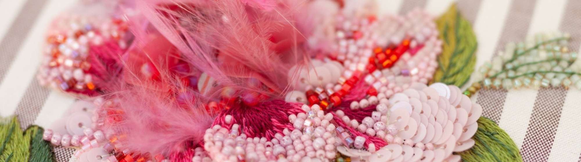 Broderie florale en relief avec perles et plumes roses sur tissu rayé.