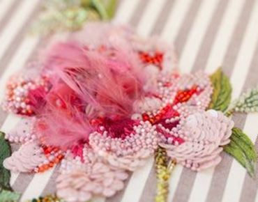Broderie florale en relief avec perles et plumes roses sur tissu rayé.