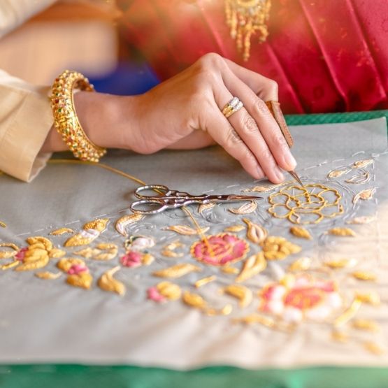 Main réalisant une broderie traditionnelle avec fil doré et motif floral.