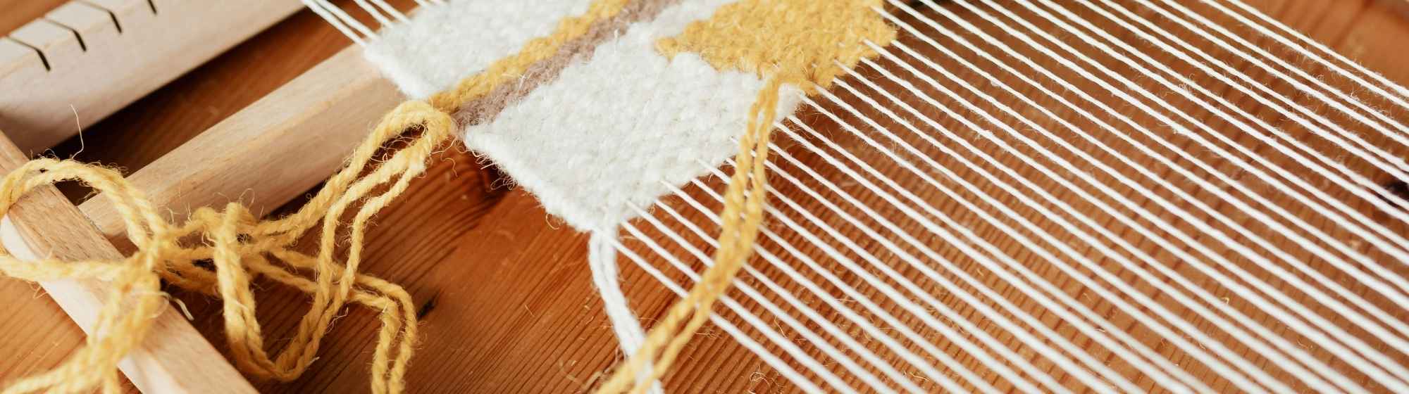 Tissage terminé sur un métier à tisser avec fils de laine jaune et blanc.
