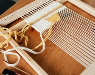 Tissage terminé sur un métier à tisser avec fils de laine jaune et blanc.