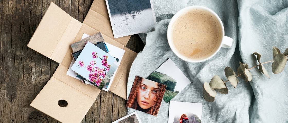 Sélection de petites photos imprimées et posées à côté d’un café sur une table en bois.