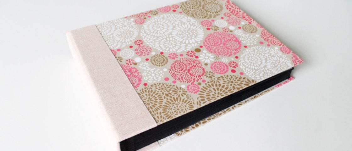 Album photo fermé avec une couverture cartonnée décorée de motifs floraux roses, blancs et dorés.