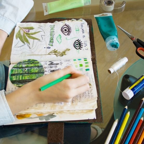 Main coloriant un art journal rempli de dessins, collages et notes créatives.