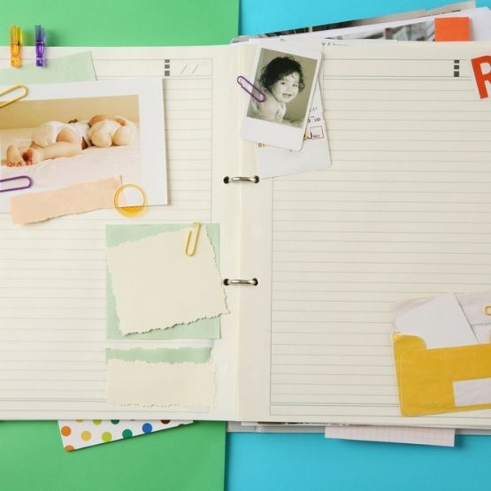 Carnet ouvert avec des photos, papiers colorés et notes attachés par des trombones.