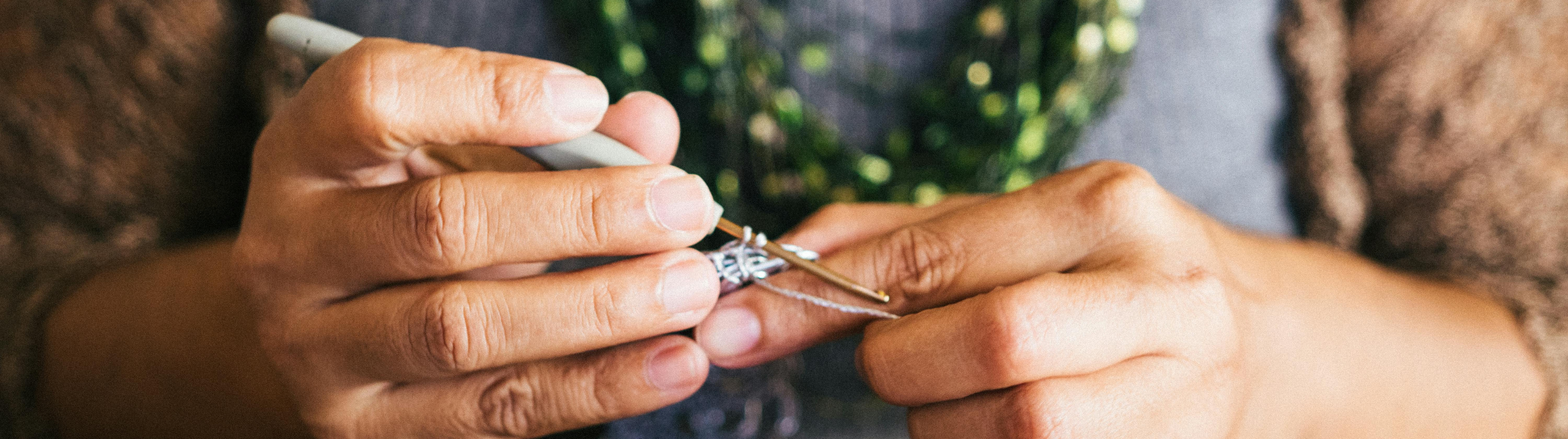 Mains en train de crocheter avec un fil métallisé argenté, sur une table en bois.