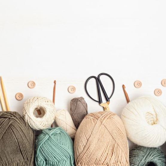 Panier contenant des pelotes de laine naturelles et une pièce en cours de tricotage avec des aiguilles.