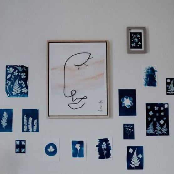 Affichage mural d'œuvres en cyanotype bleu et blanc autour d'une illustration minimaliste encadrée.