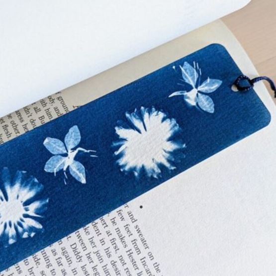 Marque-page en cyanotype inséré dans un livre, orné de motifs végétaux blancs sur fond bleu.