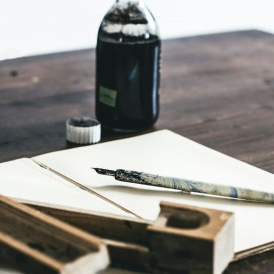 Flacon d’encre végétale et plume posés sur une table en bois avec du papier.