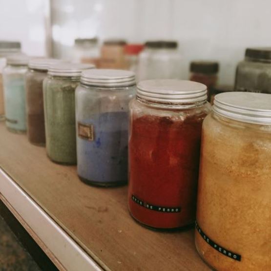 Bocaux contenant différents pigments naturels colorés alignés sur une étagère.