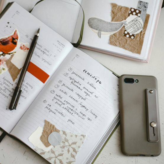 Carnets ouverts avec collages créatifs et liste manuscrite, à côté d’un smartphone.