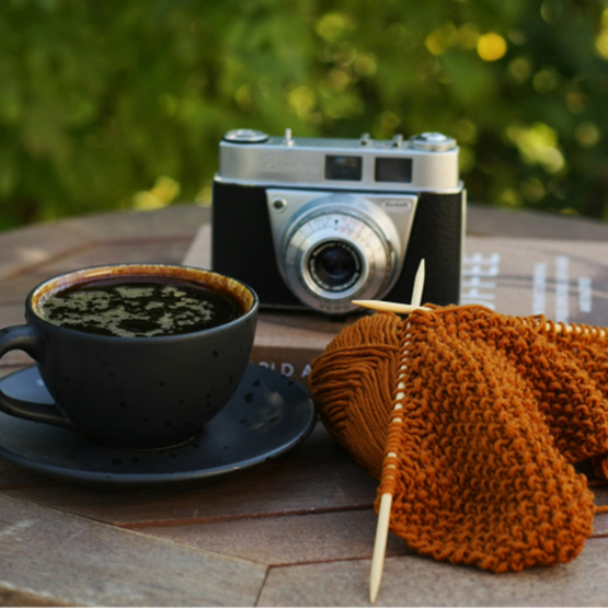 Tasse de café, tricot en cours et appareil photo vintage sur une table en bois.