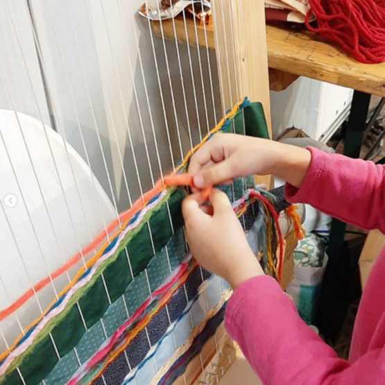 Enfant en train de tisser des fils colorés sur un métier à tisser.