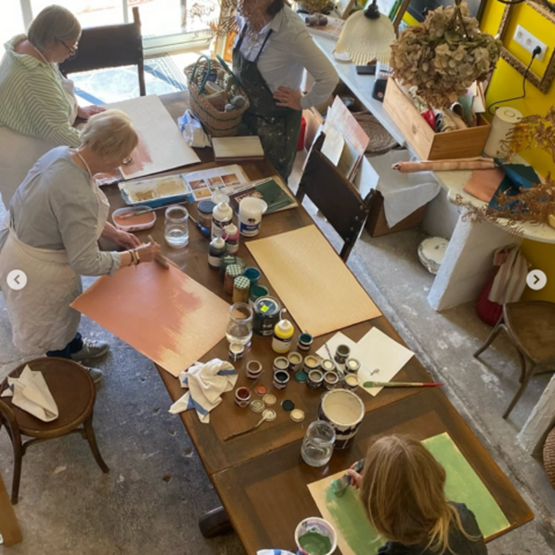 Vue plongeante d’un atelier créatif avec plusieurs personnes peignant autour d’une grande table.
