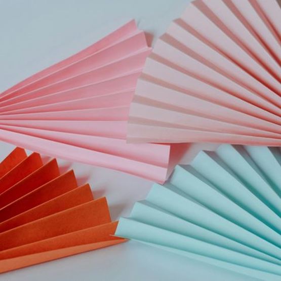 Ensemble d’éventails en papier coloré pliés en accordéon sur fond blanc.