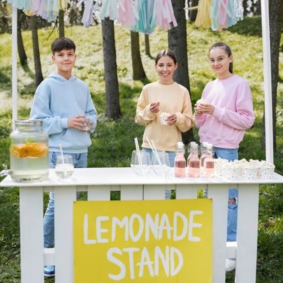 Trois enfants vendent de la limonade dans un stand coloré en plein air.