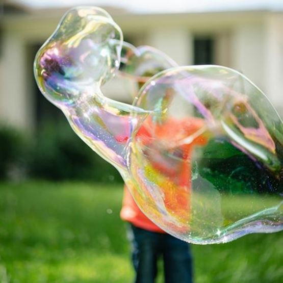 Bulles de savon géantes devant un enfant flou en arrière-plan dans un jardin.