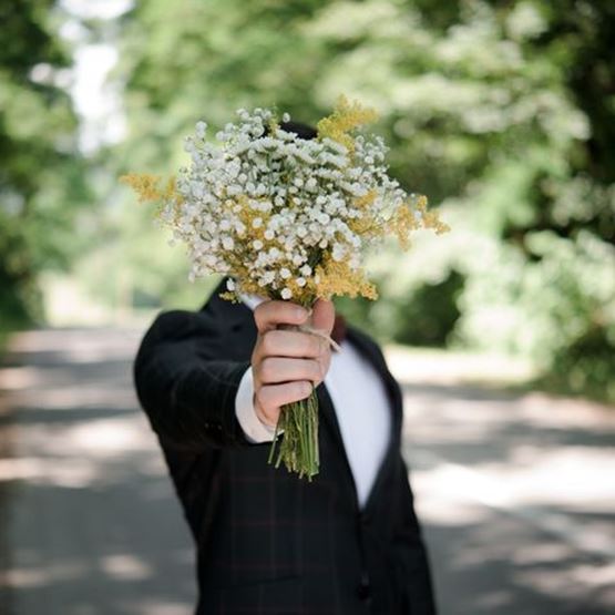 Marié tenant un bouquet de gypsophile et de fleurs jaunes devant lui, visage caché.
