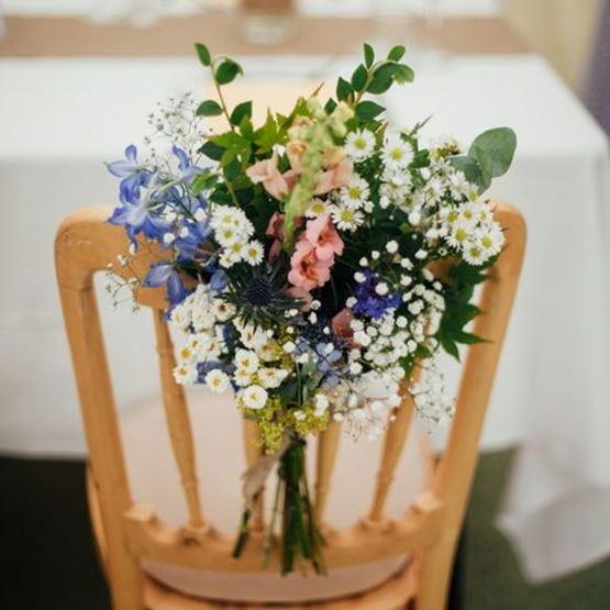 Bouquet champêtre attaché au dossier d’une chaise en bois pour un mariage.