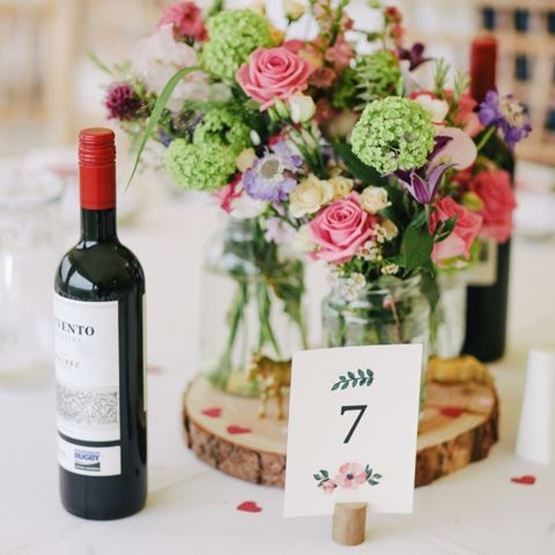 Centre de table de mariage avec fleurs fraîches, bouteille de vin et numéro de table.