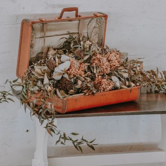 Vieille valise orange remplie de fleurs séchées, posée sur une table rustique.