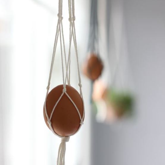 Œuf suspendu dans un filet en macramé blanc, accroché devant une fenêtre.