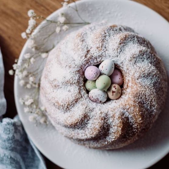 Gâteau de Pâques en couronne saupoudré de sucre glace, garni d'œufs en chocolat pastel au centre.