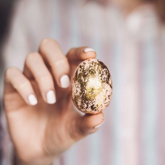 Main féminine tenant un œuf de Pâques décoré de feuilles d’or.