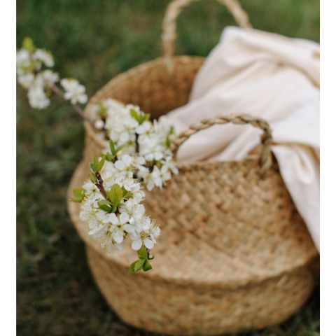 Panier en osier contenant un tissu beige et une branche de fleurs blanches.