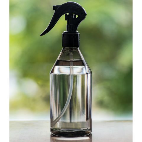 Flacon pulvérisateur transparent posé sur une surface brillante avec un fond flou vert.