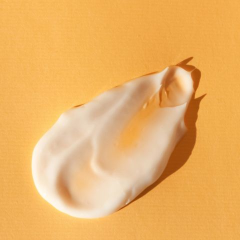 Texture de crème blanche avec une touche dorée sur un fond orange pastel.