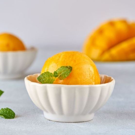 Sorbet à la mangue servi dans une petite coupelle blanche avec feuille de menthe.