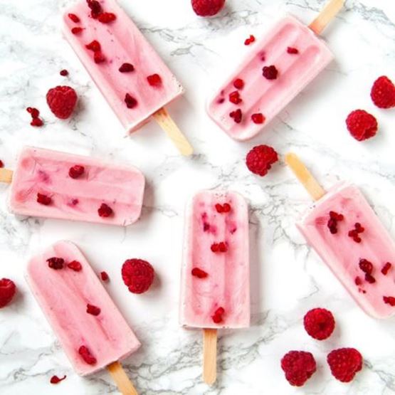 Glaces à l’eau roses avec morceaux de framboises, posées sur fond marbré.