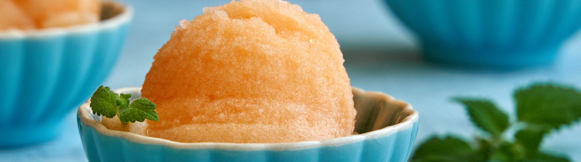 Quatre cornets de sorbet colorés avec des fruits assortis sur fond noir.