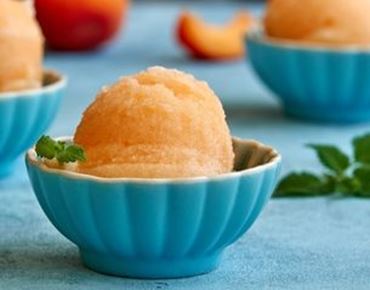 Quatre cornets de sorbet colorés avec des fruits assortis sur fond noir.