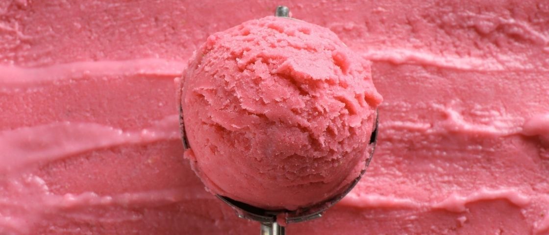 Grosse boule de sorbet rose posée sur une surface de sorbet étalé.