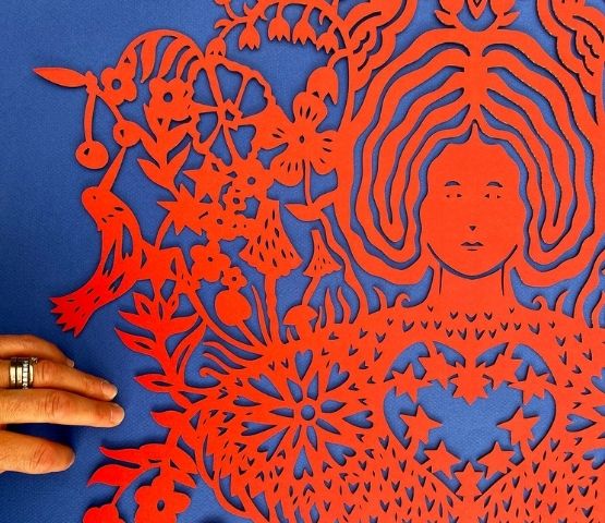 Découpe papier rouge représentant un visage féminin entouré de fleurs.