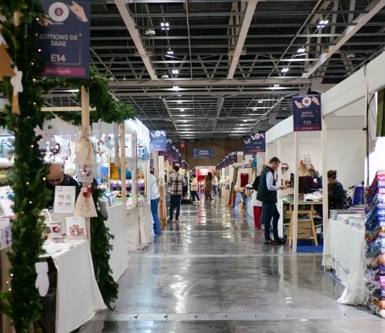 Vue d’un salon avec des stands décorés et une signalétique claire indiquant les allées et les espaces.