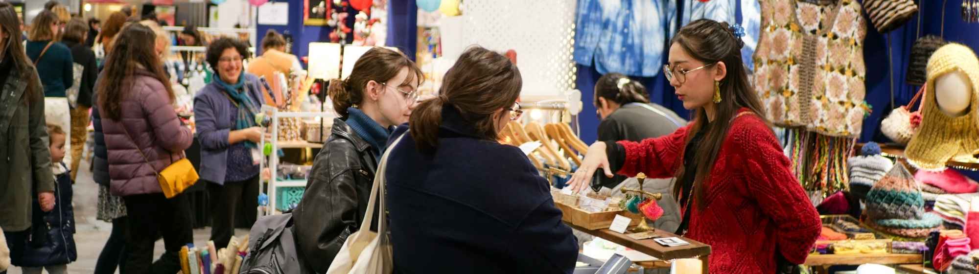 Allée d’un salon créatif avec visiteuses découvrant les stands d’artisanat.