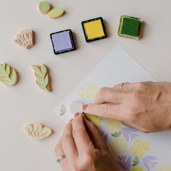 Mains en train de tamponner des motifs floraux sur une feuille à l’aide de tampons et d’encres colorées.