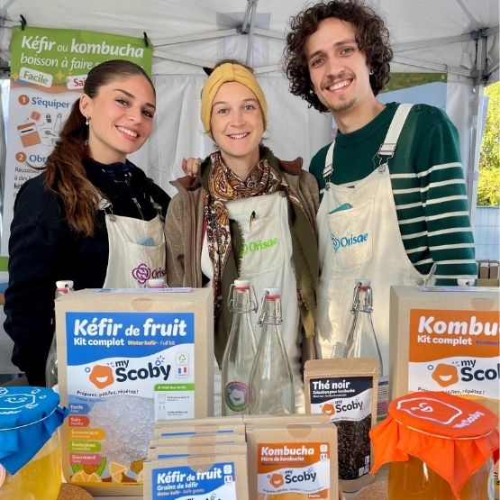 Trois personnes souriantes derrière un stand présentant des kits maison de kéfir et kombucha de la marque My Scoby.