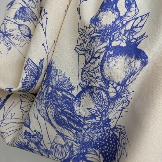 Tissu blanc imprimé de motifs floraux et fruités en encre bleue.