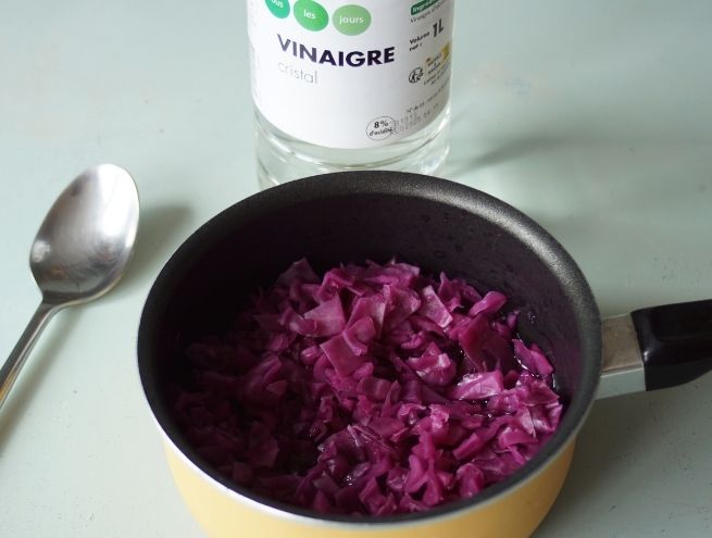 Chou violet cuit dans une casserole avec une bouteille de vinaigre à l’arrière-plan.