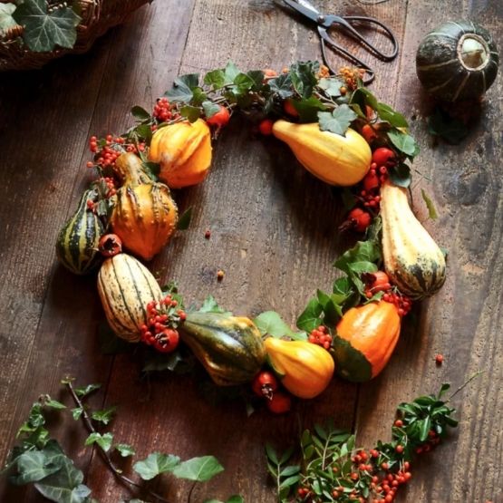 Couronne décorative d’automne composée de mini-citrouilles, baies rouges et feuillage vert.