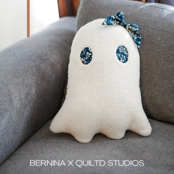 Coussin fantôme en tissu polaire blanc avec nœud bleu, posé sur un canapé.